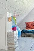 White, wood-clad attic room with stylised hunting trophy on wall and colourful covers and pillows on bed in background
