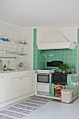 Kitchen counter with white base cabinets and wrought iron cooker and extractor hood in green-tiled cooking area