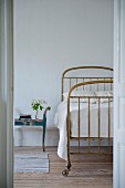 Brass bed on casters and vintage bedside table seen through open door
