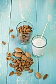 A glass of almond milk with a straw and a glass of almonds