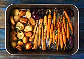 Roasted root vegetables and red onions in a roasting tin