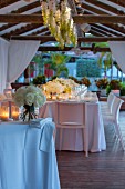 Festlich gedeckte Hochzeitstische, mit Windlichtern und Blumensträussen auf überdachter Terrasse