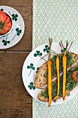 Slices of bread topped with pesto and roasted carrots on a plate with a clover leaf pattern