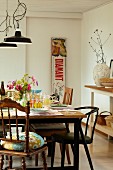 Set table, various chairs, vintage advertising panel and open shelving in country-house interior