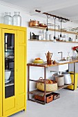 Gelber Schrank mit Glastür neben Küchenzeile mit Holzplatte auf Metall Untergestell