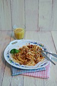 Spaghetti Bolognese auf Porzellanteller mit Basilikumblatt, Orangensaft im Glas