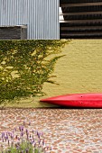 Red canoe leant against yellow brick courtyard wall