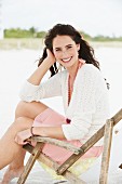 A brunette woman sitting in a deck chair wearing a summer dress and a cardigan