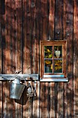 Row of hooks next to small lattice window in façade of wooden house in pattern of light and shade