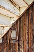 Alte Gaslaterne an Nagel unter einem Treppenlauf, dahinter Holzfassade