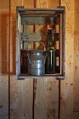 Alte Milchkanne und Flasche mit Bügelverschluss als Deko in Obstkiste an der Wand eines Holzhauses