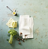 A soft-boiled egg, cheese, broccoli and a napkin on a stone surface