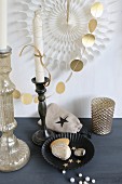 Christmas arrangement of gold-painted pebbles in black cake tin, white candle in candlestick and garland of gold paper discs