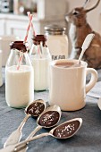 Chocolate in bowls of spoons, mug of hot chocolate and bottles of milk with drinking straws