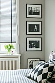 Blick über Bett mit Kissen auf schwarz-weiße Fotos an hellgrauer Wand neben Fenster