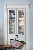 Fitted, glass-fronted cabinet with shopping bag hung from door knob