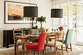 Verschiedene, gepolsterte Stühle um gedeckten Holztisch, oberhalb moderne Pendelleuchten mit anthrazitfarbenen Lampenschirmen