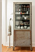 Retro vacuum cleaner next to crockery in vintage glass-fronted cabinet