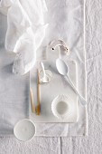Spoons, paper cases, bowls, wooden skewers and a mini cake stand on a white chopping board on a white surface