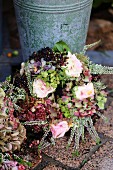 Autumnal wreath of dried hydrangeas, roses, elderberries and heather leaning against zinc bucket
