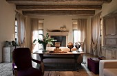 Interior of old renovated villa; rustic wooden table against back of sofa and draped, floor-length curtains on windows