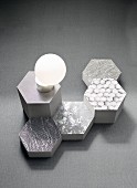 Fabric patterns on honeycomb-shaped objects in shades of grey and an opal glass lamp