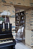 Piano in front of rustic wall with view of reading chair in library through open doorway