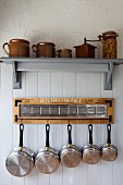 Stoneware crockery on bracket shelf above collection of stainless steel pans hanging from rack