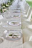 Lange Festtafel mit dekorierten Gedecken, Silberplatzteller, davor Stühle mit weisser Husse