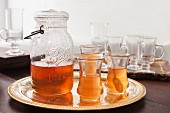 Tea in a glass jug with a handle and tea glasses on a golden tray
