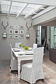 Striped, loose-covered chairs in front of antlers and pictures on wall of dining area
