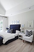 Helles Schlafzimmer mit elegantem dunkelblauem Bett, grafisch gemusterten Kissen und Bildergalerie