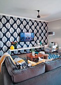 Wohnbereich mit Überecksofa und Sesseln vor Wand-TV, Tapete mit Blattmotiv