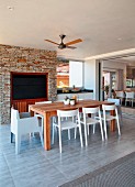 Wooden dining table and white plastic chairs on roofed terrace