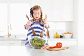 A little girl standing at the kitchen table mixing salad