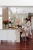 Floral armchairs at modern kitchen counter; woman arranging place settings