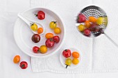Various different coloured tomatoes in a porcelain bowl and on a draining spoon
