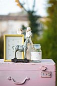 Gelber Bilderrahmen, Einmachglas und Flasche verziert mit geblümtem Papier und Pferdefigur auf rosafarbenem Vintage-Koffer