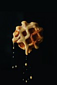 A waffle dripping with vanilla sauce