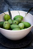Green olives with stems and leaves in a bowl on a grey wooden tray