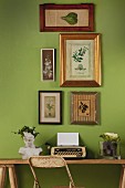 Retro Schreibmaschine und Büste vor grüner Wand mit gerahmten Pflanzenabbildungen