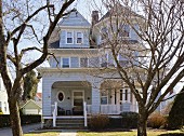 View of urban villa with pale grey clapboard façade between bare trees