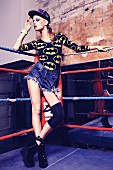 A young woman wearing denim shorts and a Batman T-shirt standing in a boxing ring