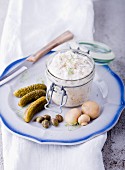 Tartar sauce in a jar on a plate with gherkins, capers and mushrooms