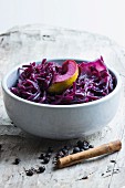 Red cabbage with apple, cinnamon and juniper berries in a grey bowl on a wooden board