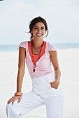 A young woman on a beach wearing a top, a shirt and a pair of white trousers