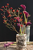 Rose hips and calla lilies in vases on wooden table
