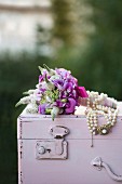Festive posy decorated with bead necklace on wooden trunk painted pastel pink