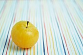 A yellow plum on a brightly coloured tablecloth