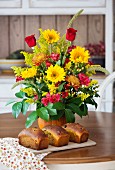 Three loaves of pumpkin bread with raisins, dried cherries and pumpkin seeds in front of a bouquet of flowers